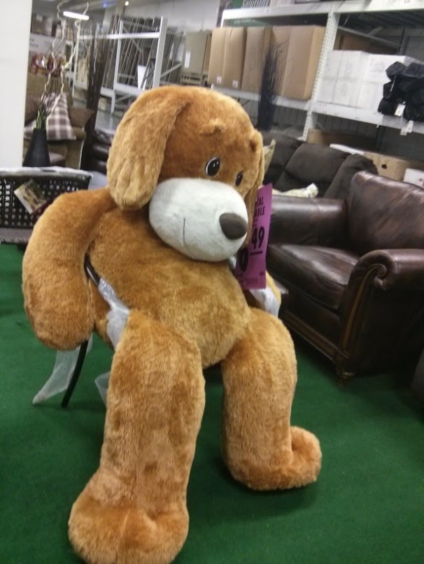 A stuffed dog so large it's spilling out of a full-sized chair.