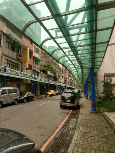 A Taipei street, with a narrow sidewalk sheltered by a greenish awning.