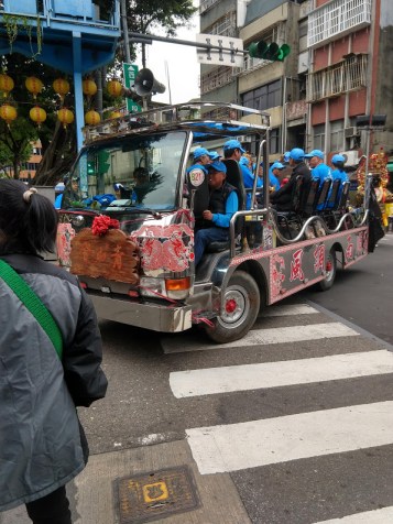 A truck with an open bed and a bunch of old people in chairs. They're all wearing matching blue jackets and baseball caps.