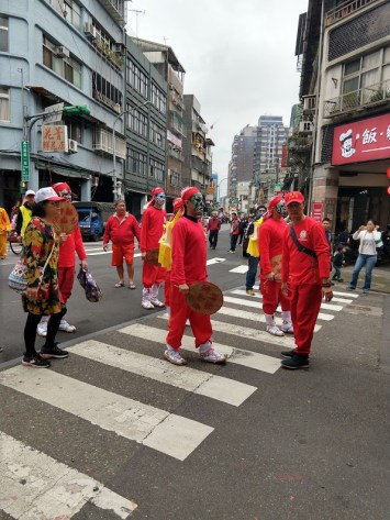 People dressed in red (long-sleeved t-shirts, sweat pants, and caps or scarves) with painted faces. Some are holding large fans.
