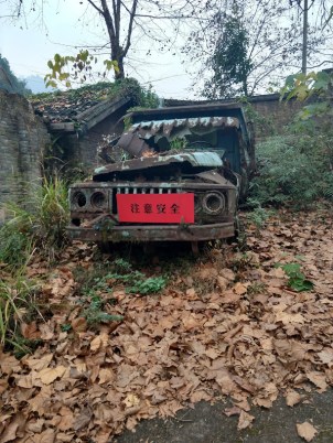 A very rusted-out truck with a red placard on the front that says something in Chinese.