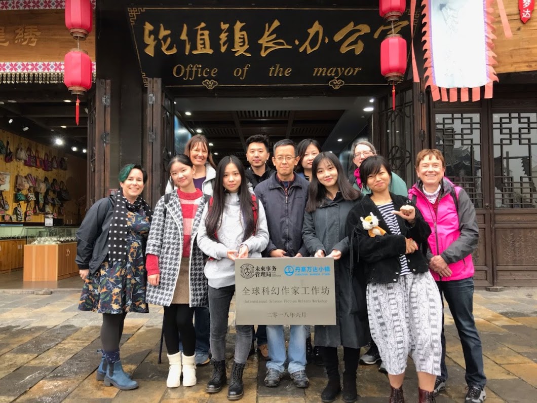 A group of writers (some Chinese, some white) holding a sign and standing in front of a building with an "Office of the Mayor" sign on it.