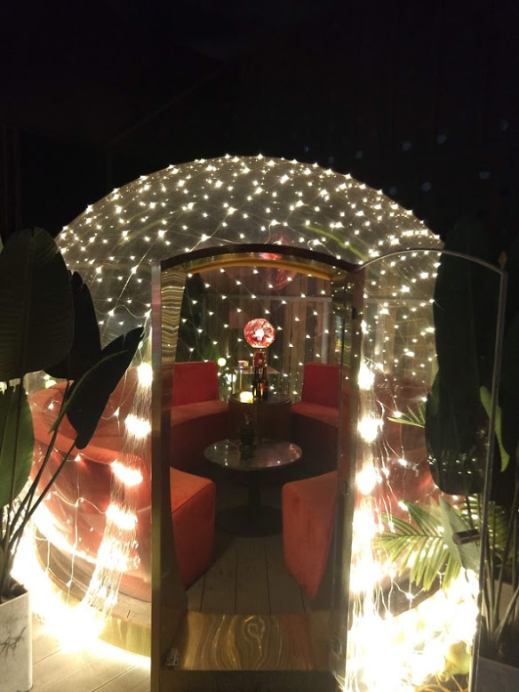 A plastic igloo thing lit up with white mini lights. Inside, you can see round bench seats around a low table.