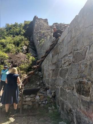 Crystal and the guide, Linda, are standing at the base of a homemade ladder leaning up against a section of the Great Wall.