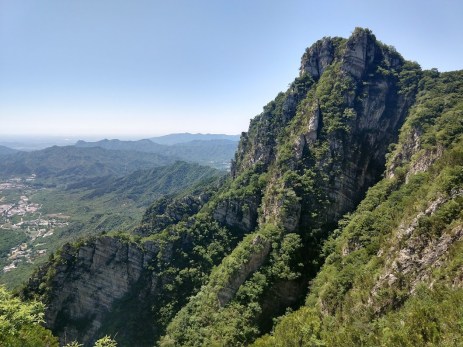 Rocky hills towering over a valley, more hills in the background, blue sky.