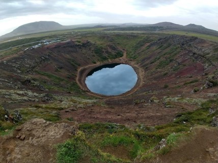 A small, very reflective and very round lake at the bottom of a steep, colorful valley.