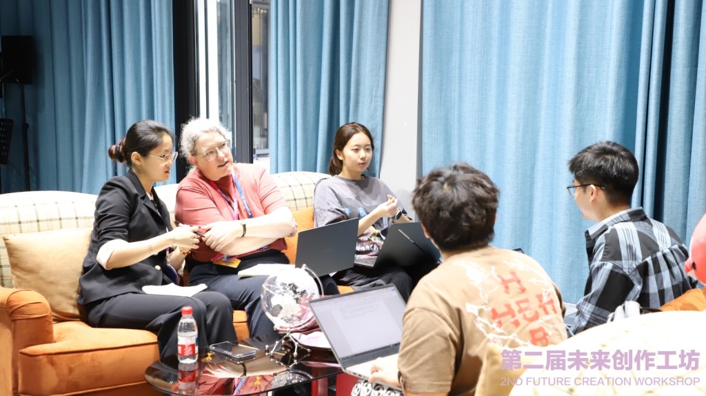 I'm on a couch. Diana is whispering in my ear; Kiki is sitting to my left. Herry and Shu and visible from behind. Everyone has a laptop out.