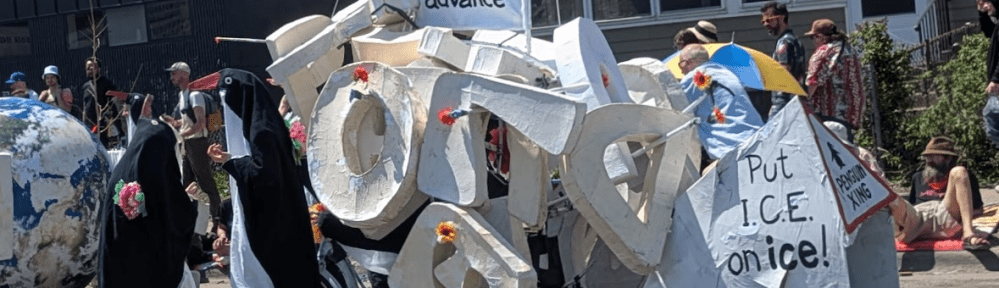 A couple of people in penguin costumes are next to a bike loaded down with papier-mache letters and signs saying "Don't Obey in Advance!" and "Put ICE on ice!"