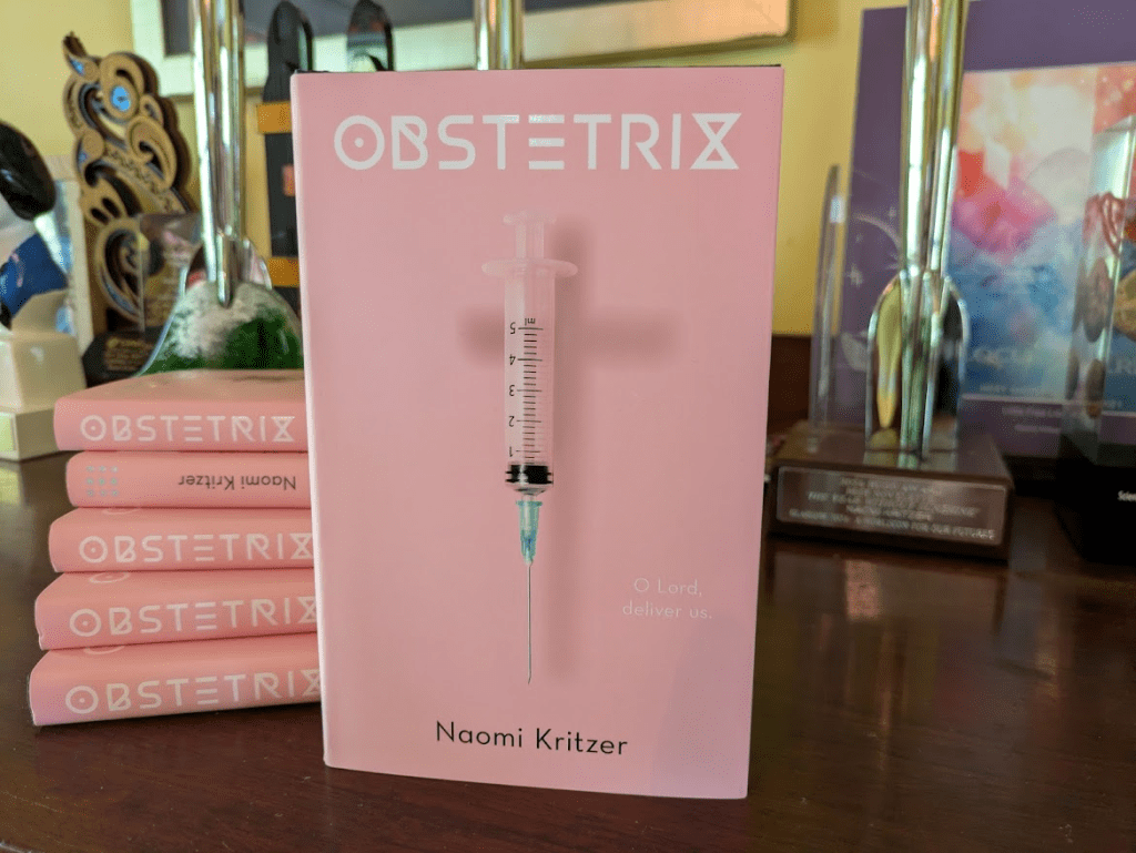 OBSTETRIX -- a pink book that says OBSTETRIX / Naomi Kritzer and has an image of a hypodermic syringe casting the shadow of a cross. In small white text it says, "O Lord, Deliver Us."